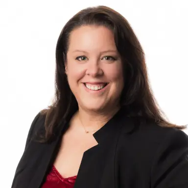Studio headshot of a woman with dark hair in a black blazer on a white backdrop