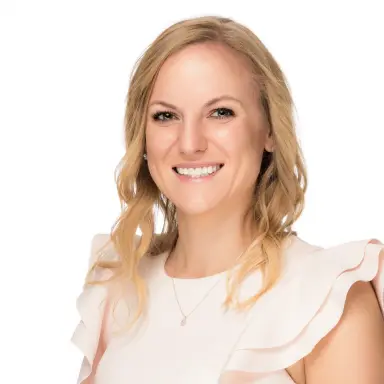 Studio headshot of a blonde woman in a cream ruffled top on a white backdrop