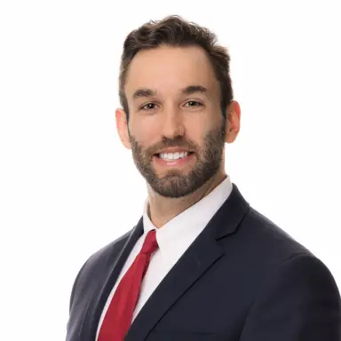 Studio headshot of a bearded man in a navy suit and red tie on a white backdrop