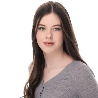 Studio headshot of a young woman with long dark hair in a gray top on a white backdrop