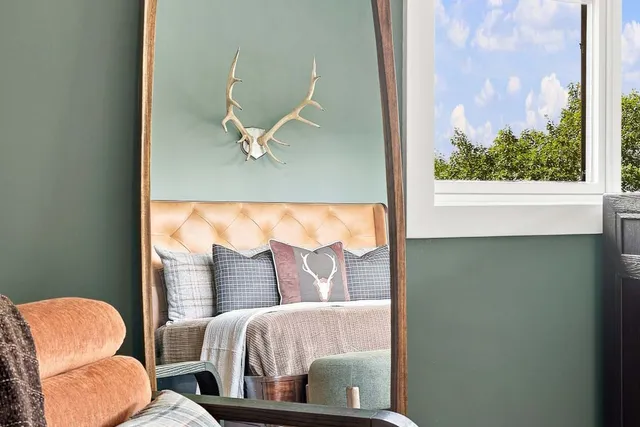The bed and mounted antlers reflected in a leaning arched floor mirror