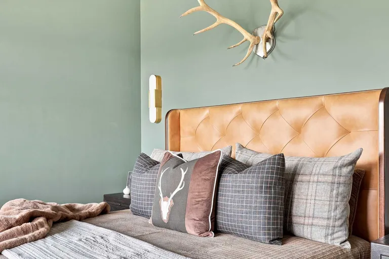 Detail of the tufted leather headboard with layered plaid pillows and a brass sconce