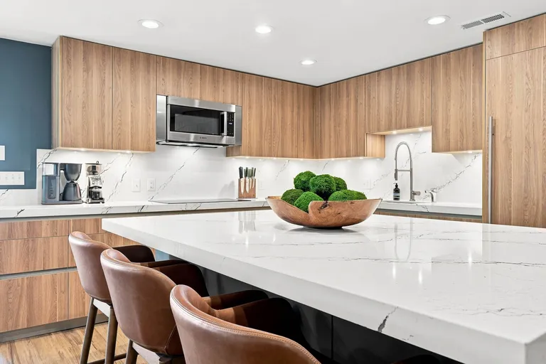 Kitchen island in a white veined stone with leather barstools and full height wood cabinetry