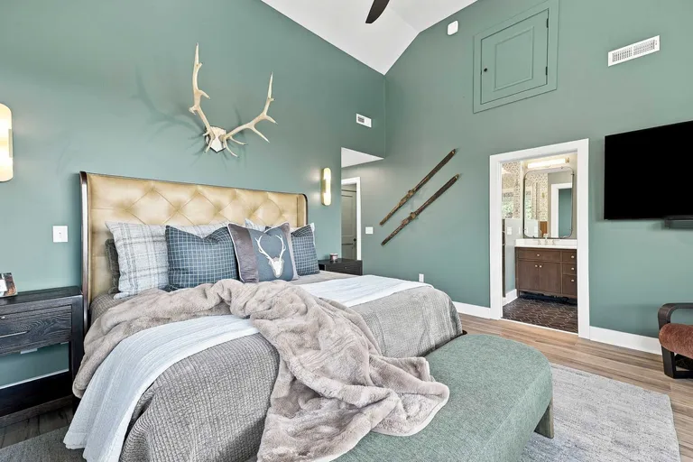 Bedroom with a camel tufted leather headboard, mounted antlers and a sage green accent wall