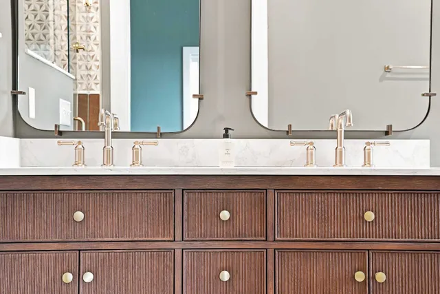 Detail of a fluted wood vanity with brass hardware under arched mirrors