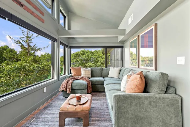 Sitting room with a green velvet sectional wrapped by windows onto the trees