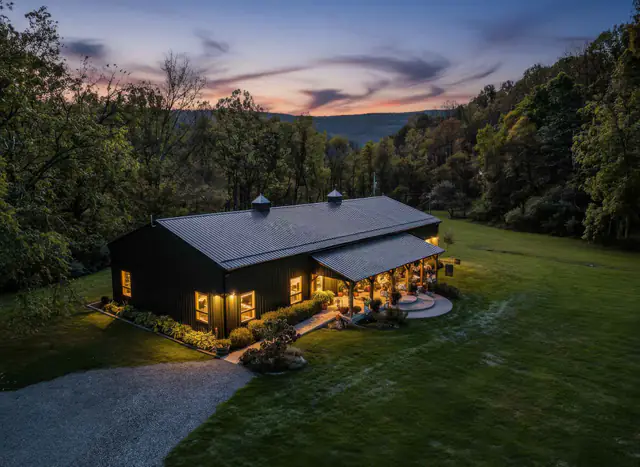 Twilight aerial photography  -  black barn venue lit at dusk below a mountain ridge